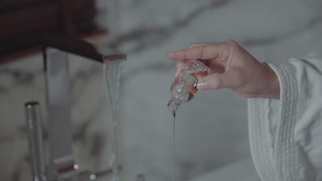 Woman's-Hand-Pouring-Clear-Liquid-Soap-Into-Bathtub-Preparing-Fresh-Bath-Soak-After-A-Long-Day