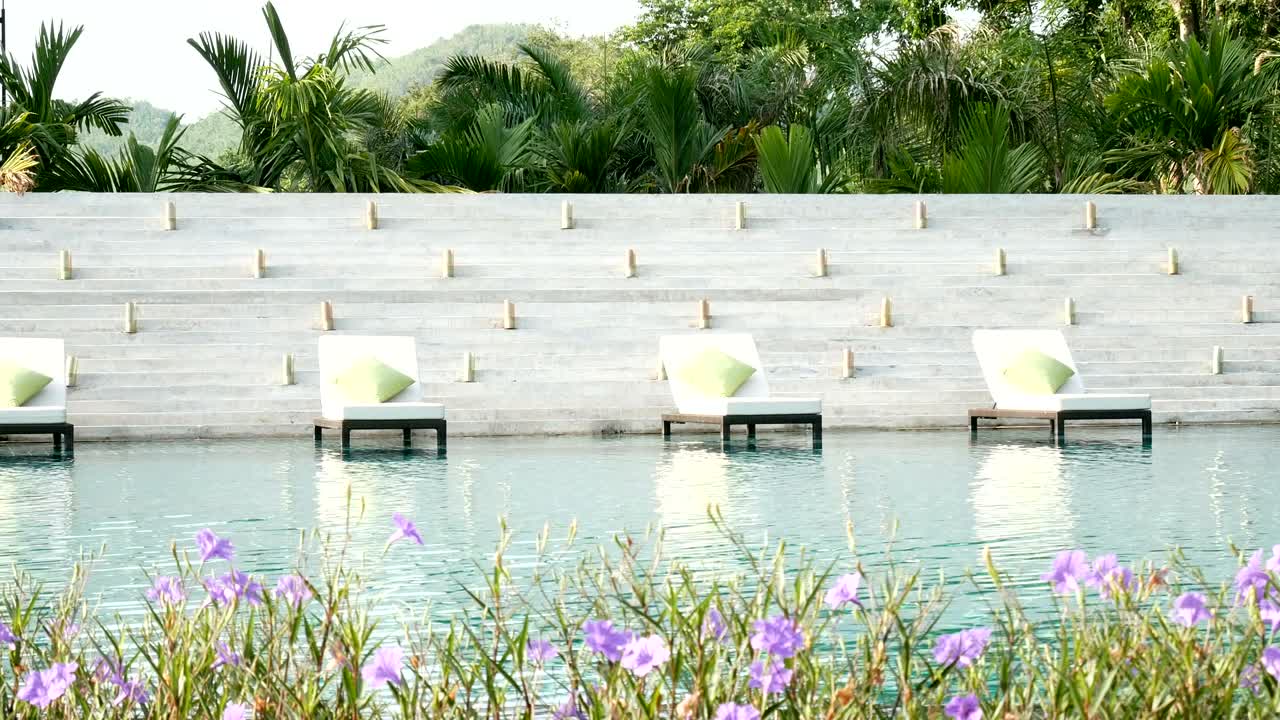 4k 원활한 루프: 자연 녹색 나무 배경과 전면에 아름다운 꽃, 사람들이 없는 수영장 근처의 누워있는 의자.