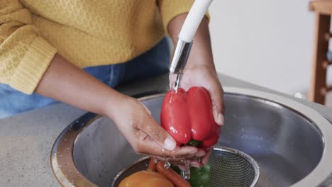 Midsection-of-african-american-woman-rinsing-vegetables-in-kitchen-sink,-slow-motion