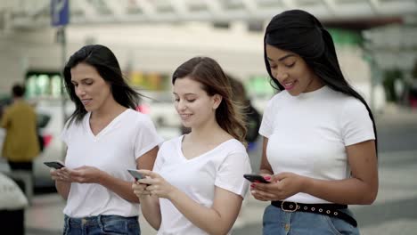 Joyful-friends-walking-on-street-with-smartphones