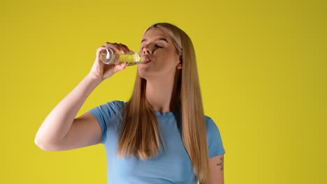 blonde woman drinking water from glass bottle, studio portrait
