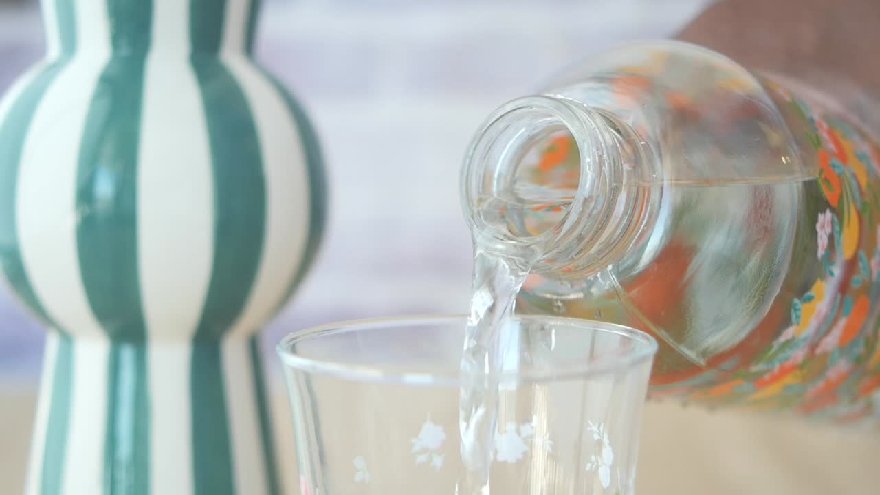 꽃 모양 의 병 에서 물 을 유리잔 에 부어 넣는 것