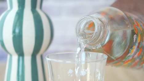 pouring water from a floral patterned bottle into a glass