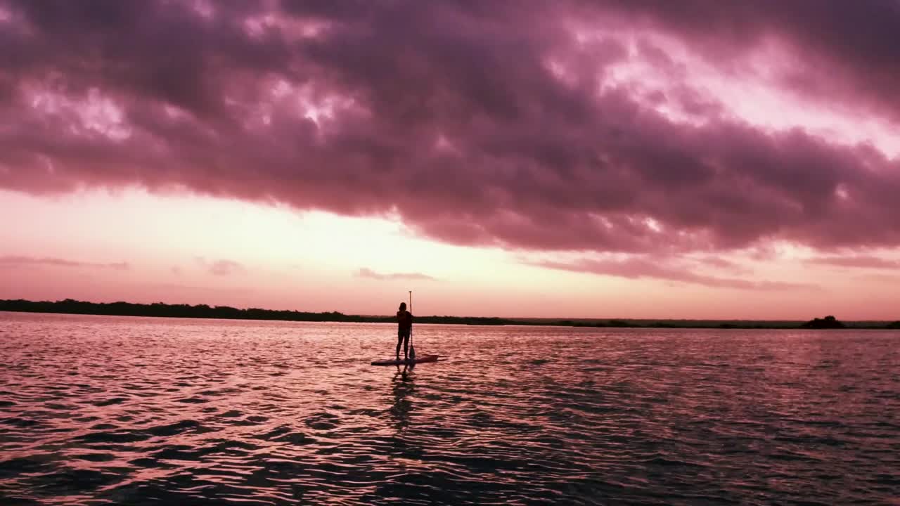 다채로운 일출 동안 호수 한가운데 그녀의 보드에 서있는 패들 보더