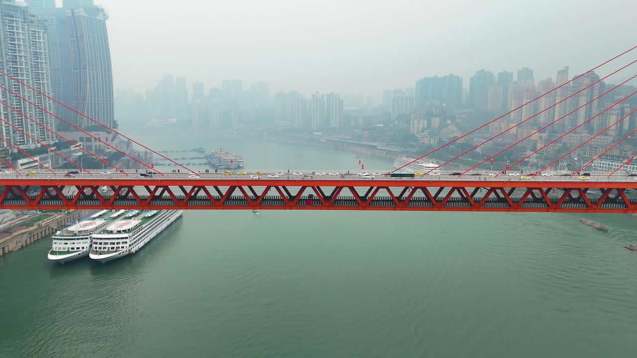 The Dongshuimen Bridge in Chongqing, China, spans the Yangtze River. A striking red suspension bridge with an urban skyline backdrop, showcasing modern infrastructure over a river.