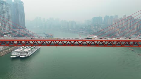 the dongshuimen bridge in chongqing, china, spans the yangtze river. a striking red suspension bridge with an urban skyline backdrop, showcasing modern infrastructure over a river.