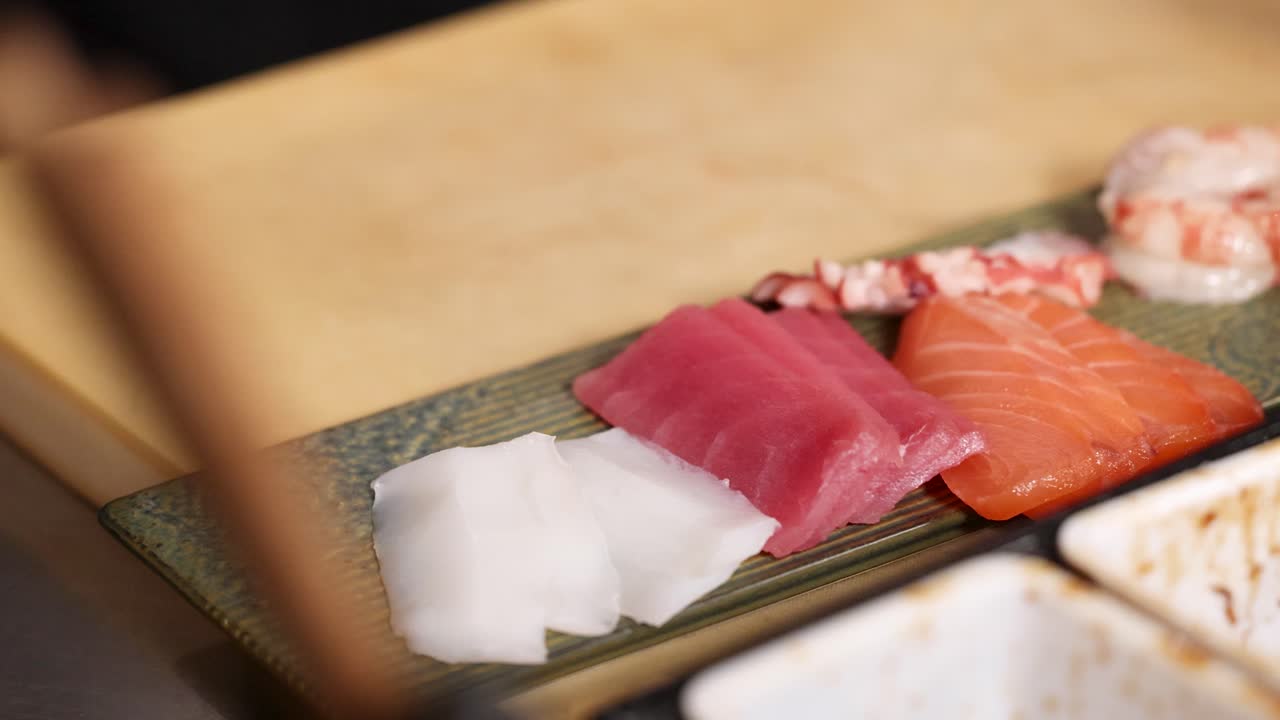 Close-up of a chef's hands carefully arranging raw tuna, salmon, and white fish sashimi