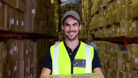 trabajador de almacén sonriendo a la cámara llevando una caja