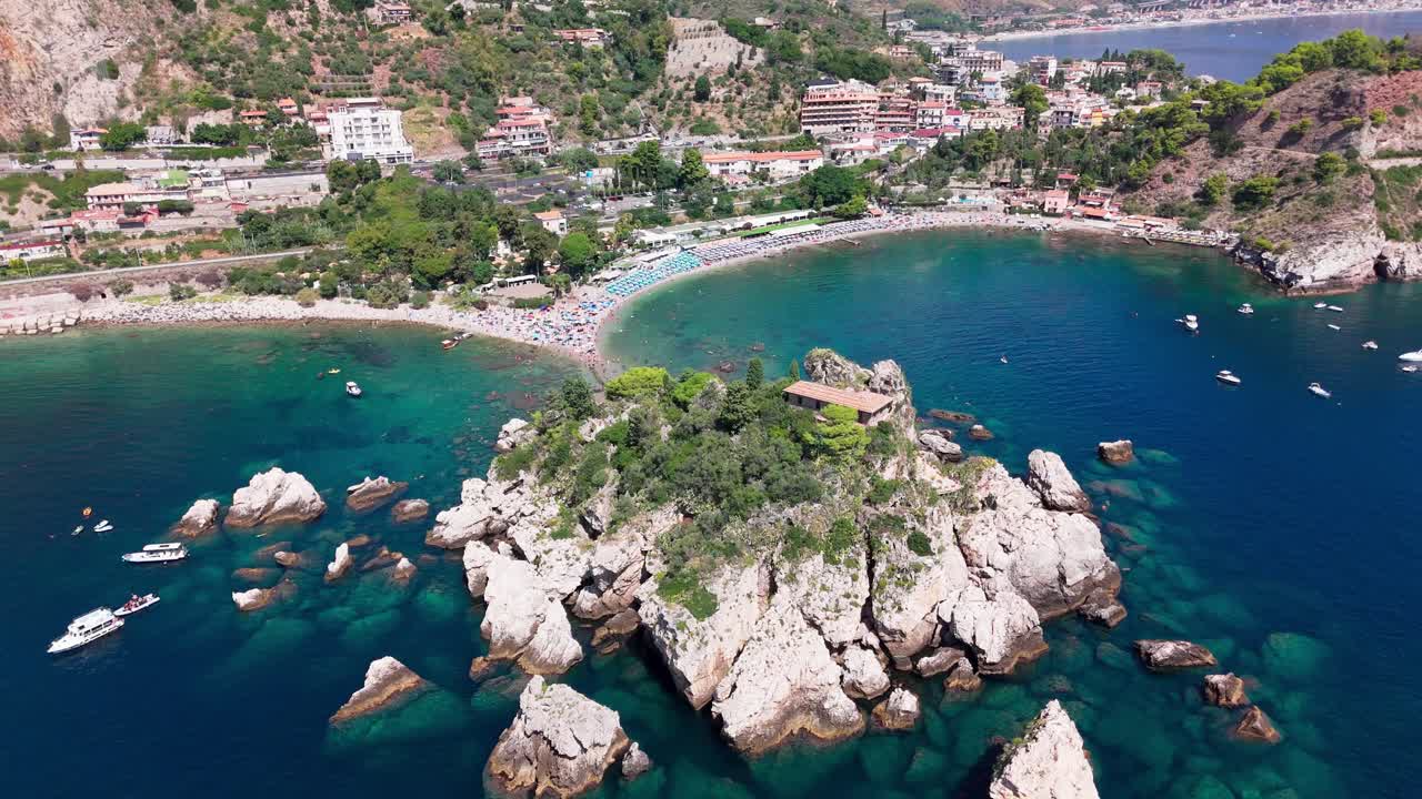 Drone pans close around Isola Bella, showing crystal-clear waters, rocky coastline, and island features in a detailed aerial shot