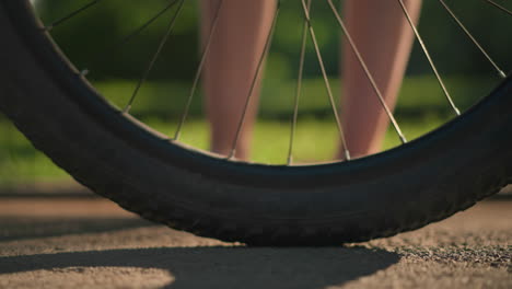 close-up of individual legs in pink sneakers kicking a bicycle tire to check air pressure, casting playful shadows on the ground, with a blurred car passing by