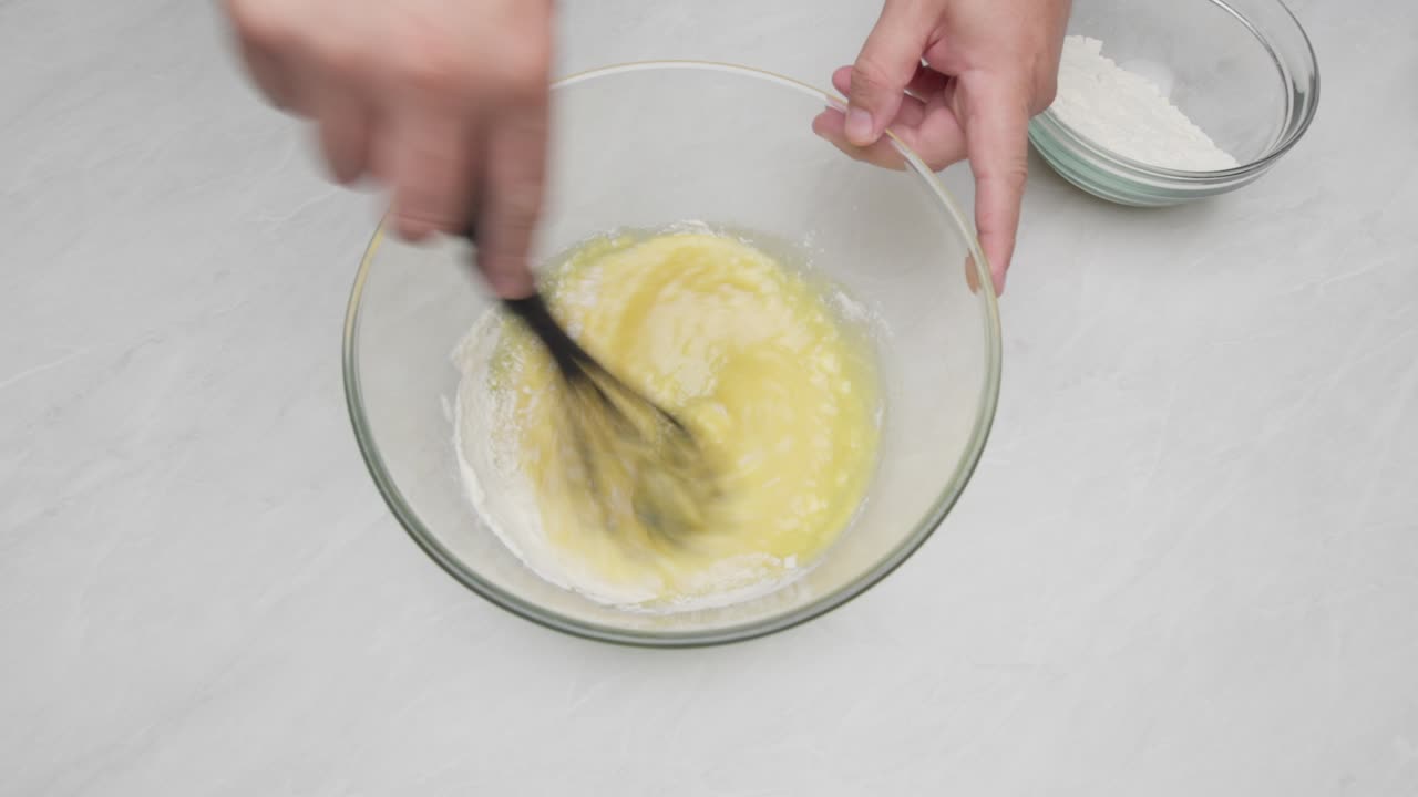 Flour is added to a glass bowl and mixed with a whisk to prepare lemon cake batter