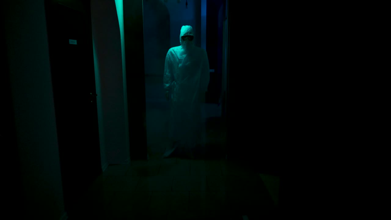 Karanlık bir koridorda koruyucu giysili kişi