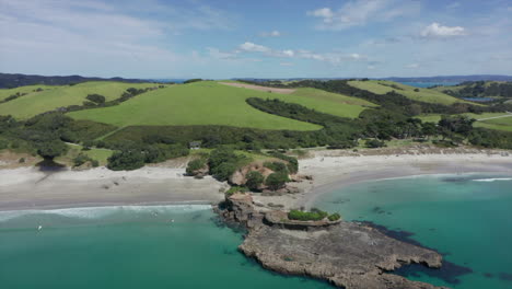 Sobrevolando-El-Agua-Azul-Cristalina-Del-Océano-Pacífico-Con-Una-Vista-Panorámica-Del-Parque-Regional-Tawharanui-En-Auckland,-Nueva-Zelanda-En-Verano