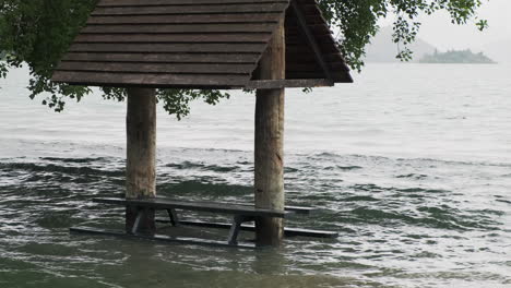 banco del parque sumergido en el agua de la inundación por un lago sereno en un día nublado