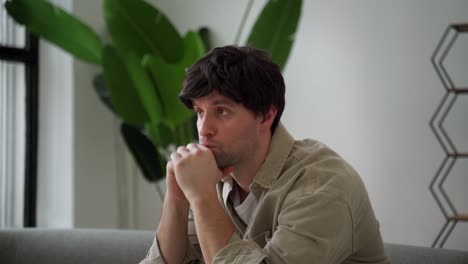 worried, sad man is worried while sitting on the couch holding his head in the living room