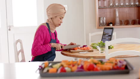 mujer biracial en hijab lavando comida en la mesa en casa con espacio de copia, cámara lenta