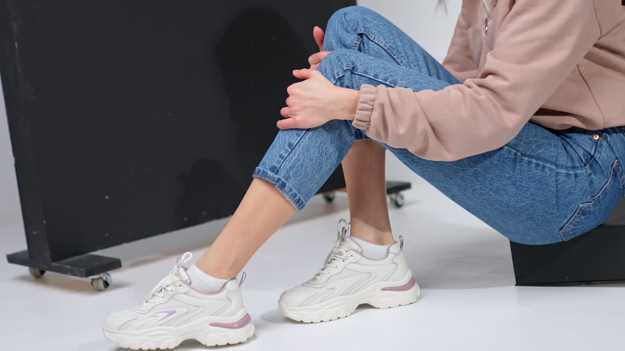 Unrecognized female model in a stylish casual look. Girl wears blue jeans, pink sweatshirt and white sneakers. Studio shot.