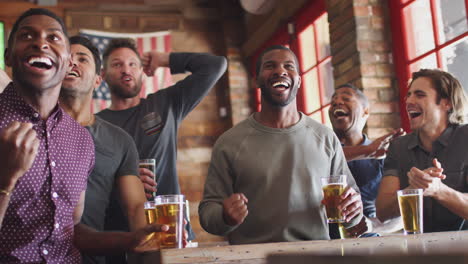 Grupo-De-Amigos-Varones-Celebrando-Mientras-Ven-El-Juego-En-La-Pantalla-En-El-Bar-Deportivo