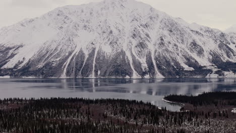 panorama of snowy mountains, forest and frozen kathleen lake in yukon, canada. - aerial tilt up shot