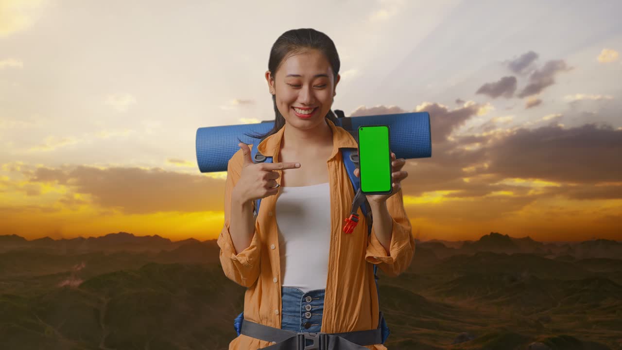 un turista feliz mostrando un teléfono de pantalla verde en una puesta de sol de montaña