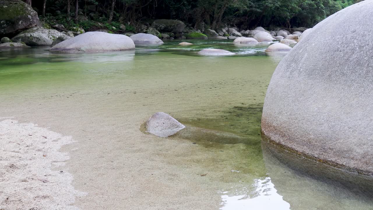 Clear water flows over rocks in a lush rainforest creek, creating a tranquil and natural setting with soft lighting