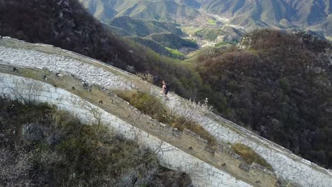 Aerial-follows-male-tourist-running-on-the-Great-Wall,-remote-section