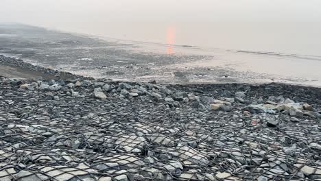 Cinematic-shot-of-a-stone-shoreline-stretched-to-the-coast-of-the-beach-at-sunset-in-Bengal,-India