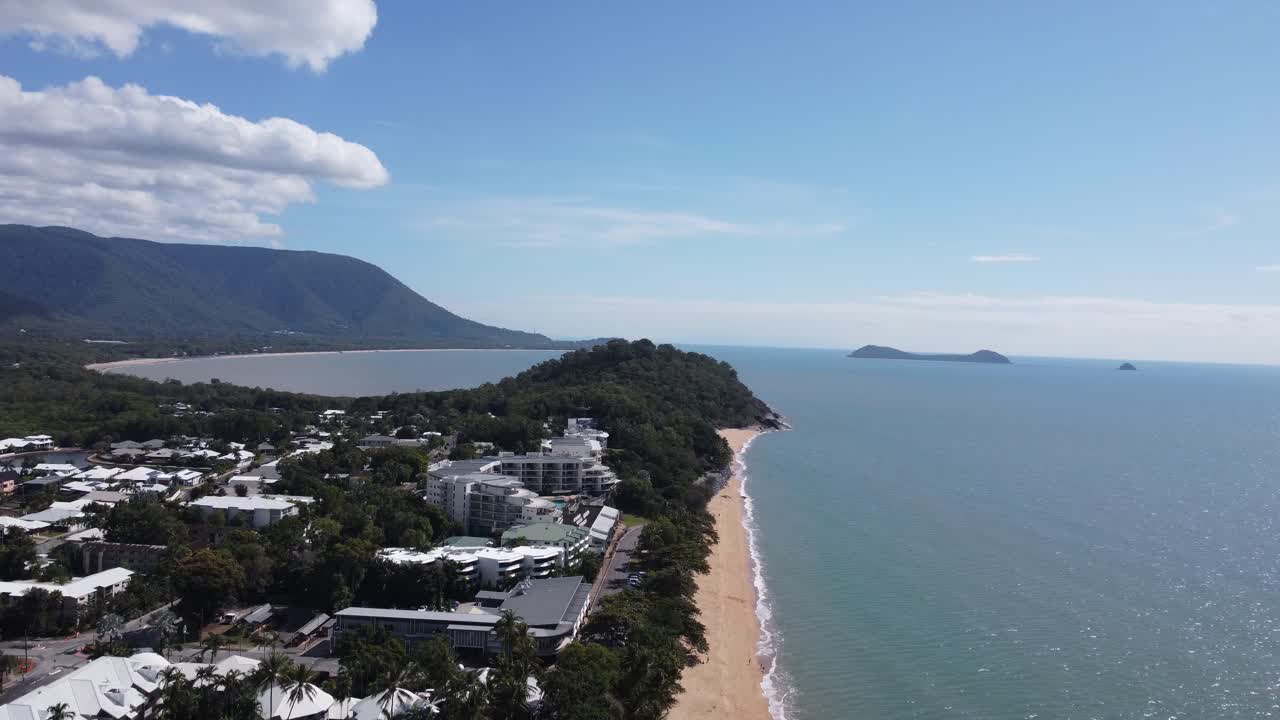 Drone ascending over a peninsula with a sandy beach, luxury beach resorts and a bay in the background in Australia