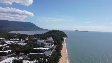 drone ascending over a peninsula with a sandy beach, luxury beach resorts and a bay in the background in australia