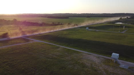 Drohne,-Die-Bei-Sonnenuntergang-Auf-Einer-Schotterstraße-Auf-Einen-Lastwagen-Oder-Ein-Auto-Zufliegt,-Und-Das-Fahrzeug-Zur-Goldenen-Stunde-Wirbelt-Viel-Staub-Auf