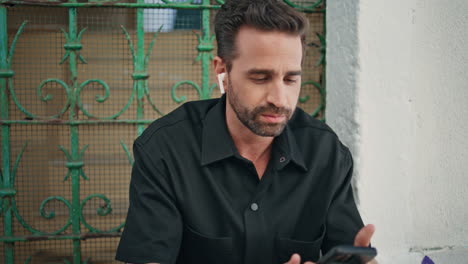 relaxed guy listening music on street in wireless earbuds closeup. man sitting