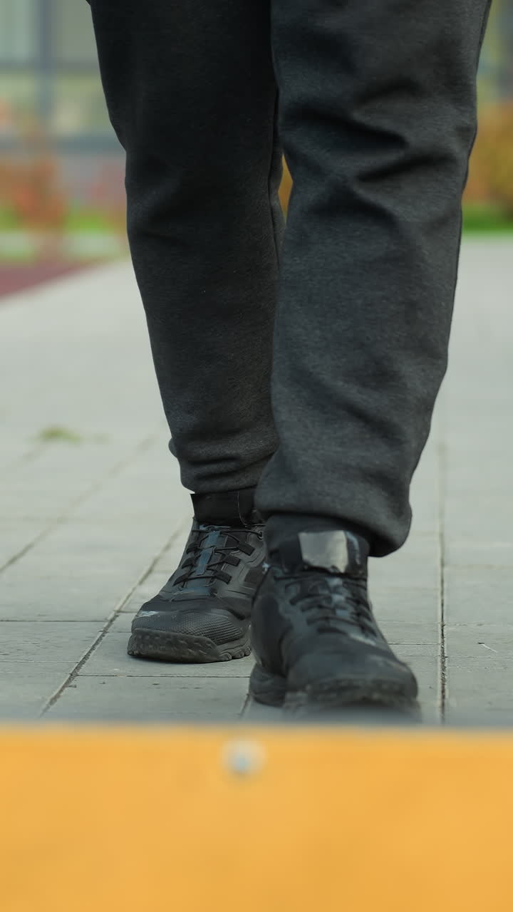 vista de la pierna de alguien entrando en una arena deportiva, mostrando la parte inferior del cuerpo y el calzado en una línea de límite amarillo vibrante, con un fondo urbano borroso
