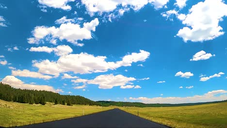 Blackbox---Driving-down-asphalt-road-in-high-mountain-treed-valley-with-blue-skies