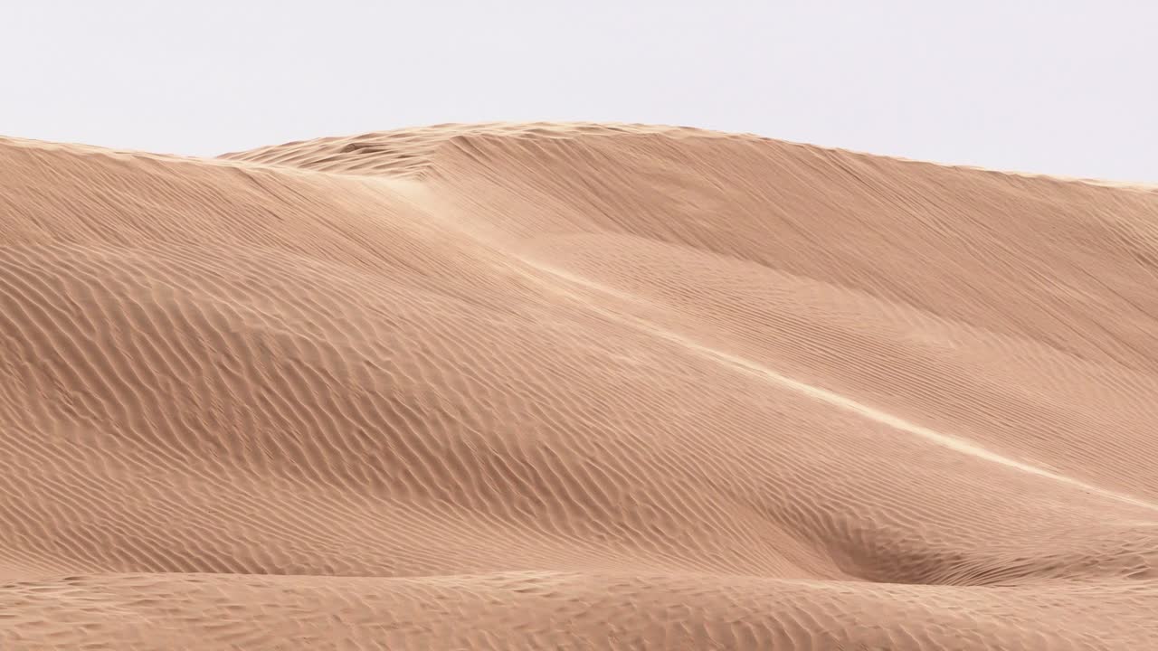 Fixed shot of golden desert sand dunes with wind blowing creating moving ripples and textured patterns showing natural landscape wilderness and arid environment under daylight