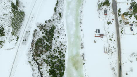 Frozen-River-Flowing-Between-Forest-And-Village-At-Haugastol-At-Wintertime-In-Norway