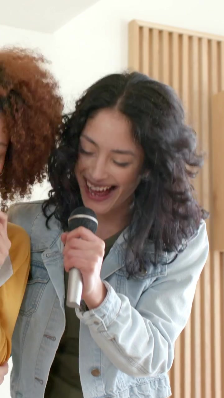 Vertical video: Reacting to beat woman in denim jacket singing into hand mic in room with partner