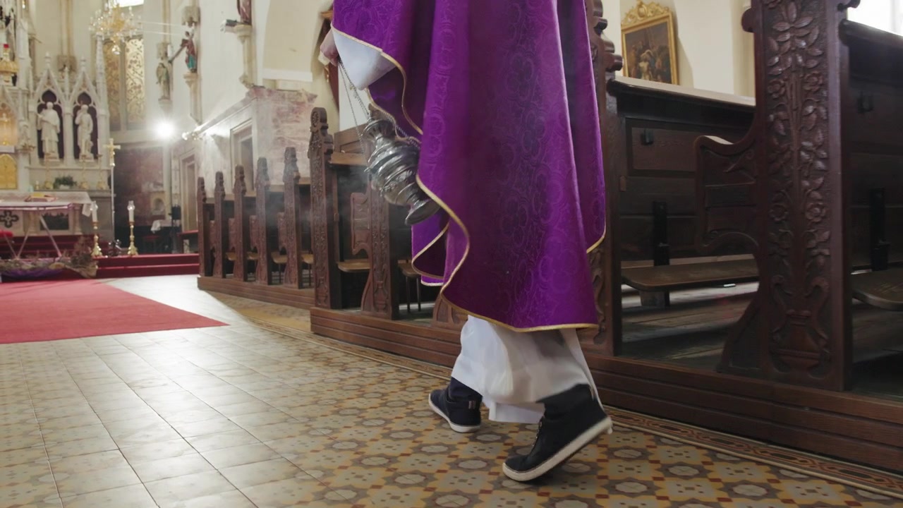 Sacerdote cattolico che porta e fa oscillare un turibolo di metallo fumante su catene mentre cammina attraverso il/la.