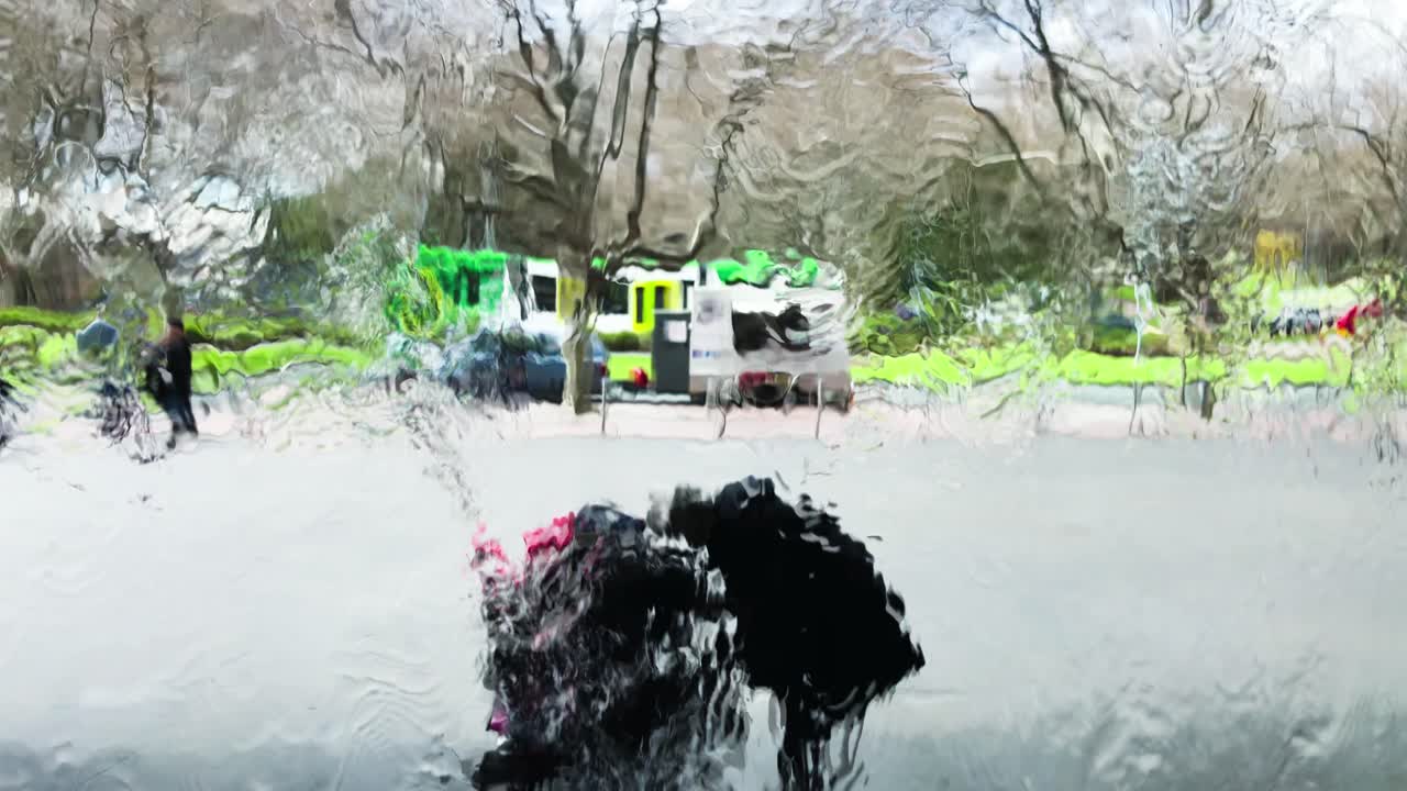 물은 유리 벽을 따라 흐르고 사람들은 물이 흐르는 유리 벽 뒤에 서 있습니다.