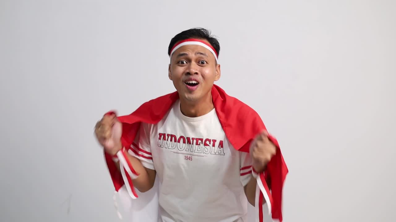 Wow surprised asian man with red white ribbon for celebrating Indonesia independence day standing while shouting with fist hands