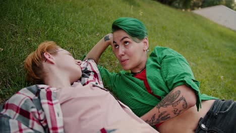 Two-lesbian-girls-with-short-bright-haircuts-in-plaid-shirts-lie-on-the-lawn-in-the-park-and-communicate-with-each-other-during-their-date