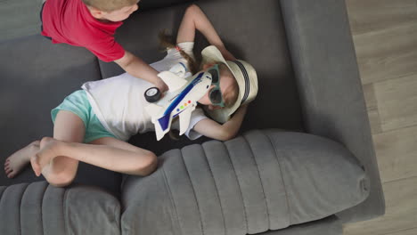 sweet girl smiles lying on sofa while little boy playing