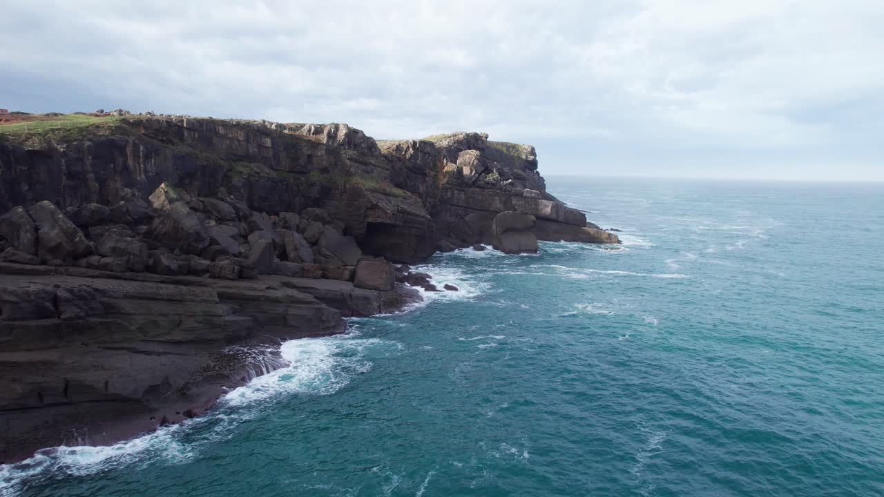 Drone che vola basso intorno a una spiaggia rocciosa sulla riva dell'oceano blu, Ajo, Cantabria, Spagna