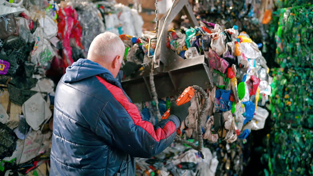 An employee stacks a cube of compressed garbage using a loader at waste sorting plant. Slow motion