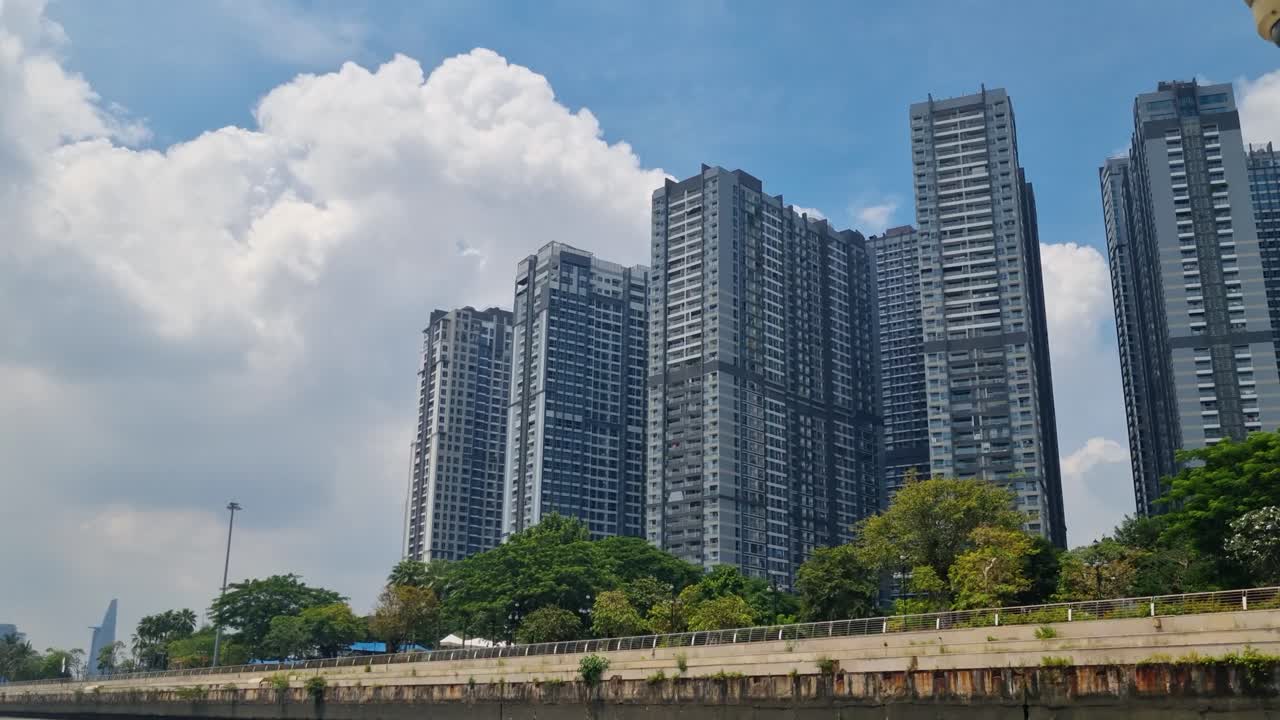 Panoramic view of Ho Chi Minh City’s skyline with modern high-rise buildings, filmed from a boat on the Saigon River under a partly cloudy tropical sky in Vietnam