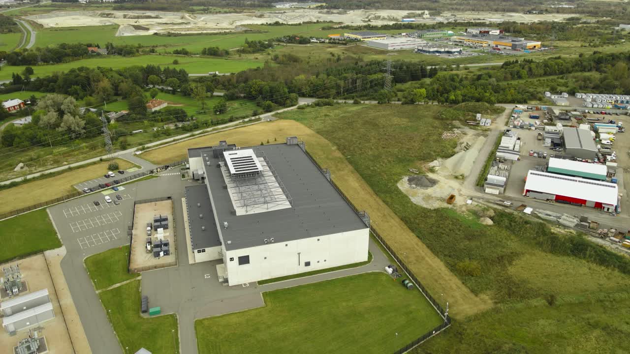 Aerial drone footage of a large AI technologies data center and server room building in a grassy green countryside with highway visible. Cooling systems and fans on the rooftop spinning. Parking lot