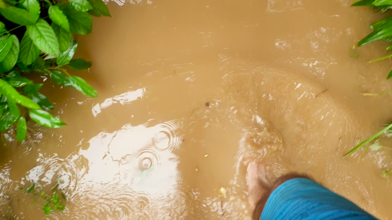 A person walking barefoot through brown muddy flood water after devastating tropical cyclone and flash flooding