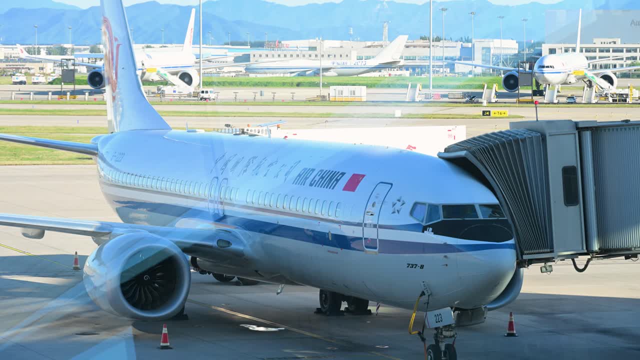 On a clear day, an Air China plane rests on the runway at Beijing International Airport, with the airport facilities and blue skies visible in the background.