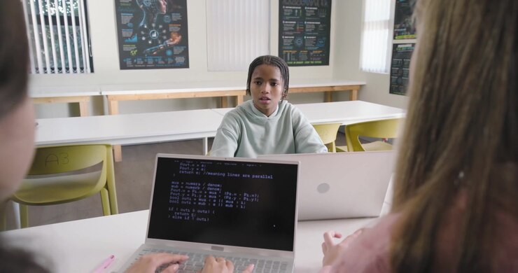 African peers typing in lab laptop showing code, leading center male in hoodie talking on project