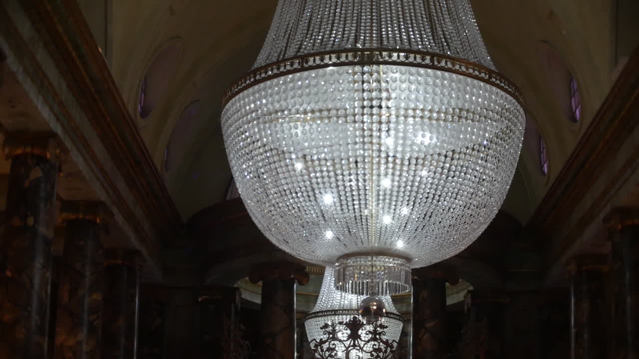 Un grande lampadario di cristallo pende maestosamente in una sontuosa sala con colonne di marmo e soffitti a volta, ideale per eventi di lusso, ospitalità di alto livello e progetti di interior design sfarzosi