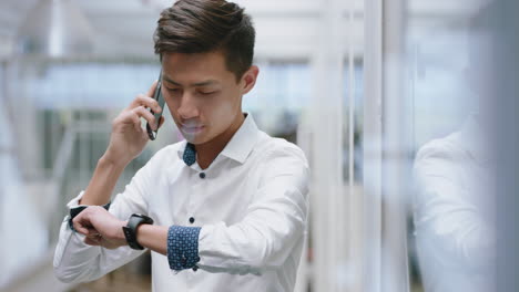 young asian businessman using smartphone having phone call chatting on mobile phone salesman enjoying conversation with client looking at wrist watch in corporate office workplace 4k